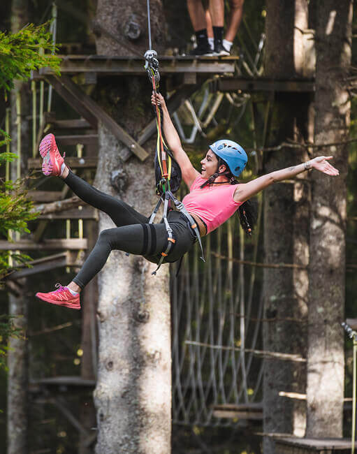 Frau mit Helm und Gurt schwebt am Seil im Kletterwald.