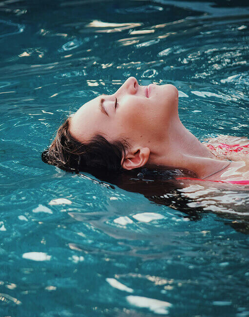 Person schwebt entspannt auf dem Rücken in blauem Wasser.