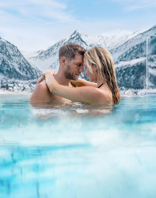 Paar umarmt sich im Wasser vor schneebedeckten Bergen.