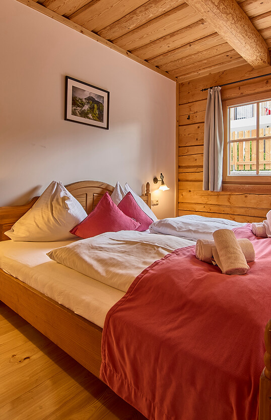 Schlafzimmer mit Holzbett, weißen/rosa Kissen, Holzdecke.