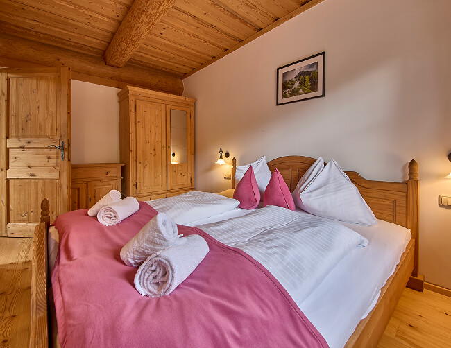 Schlafzimmer mit Holzbett, pinker Decke und Handtüchern.