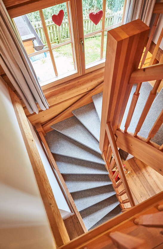 Blick von oben auf Holz-Wendeltreppe mit grauem Teppich.