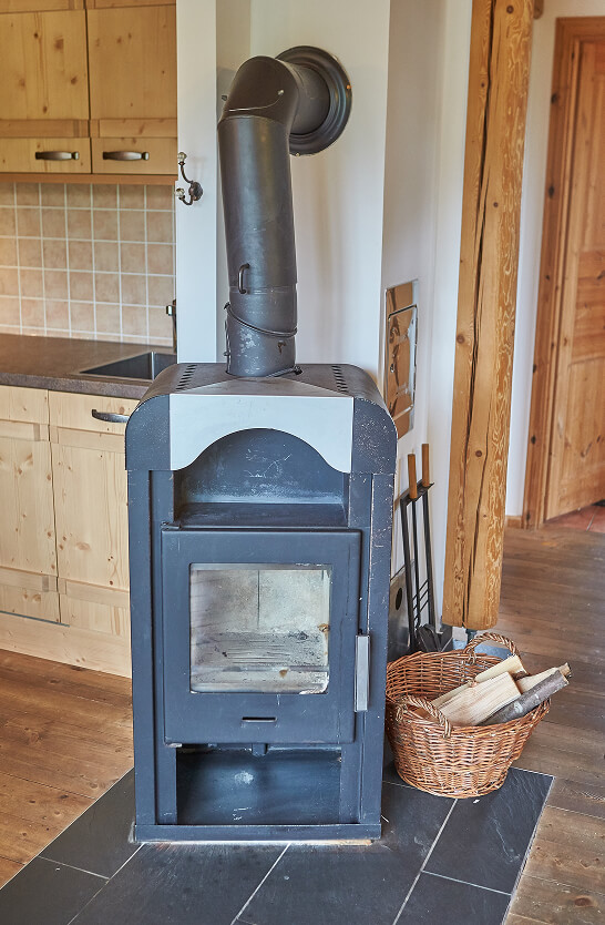 Schwarzer Kaminofen mit Glasfront, Holzkorb, Küche.