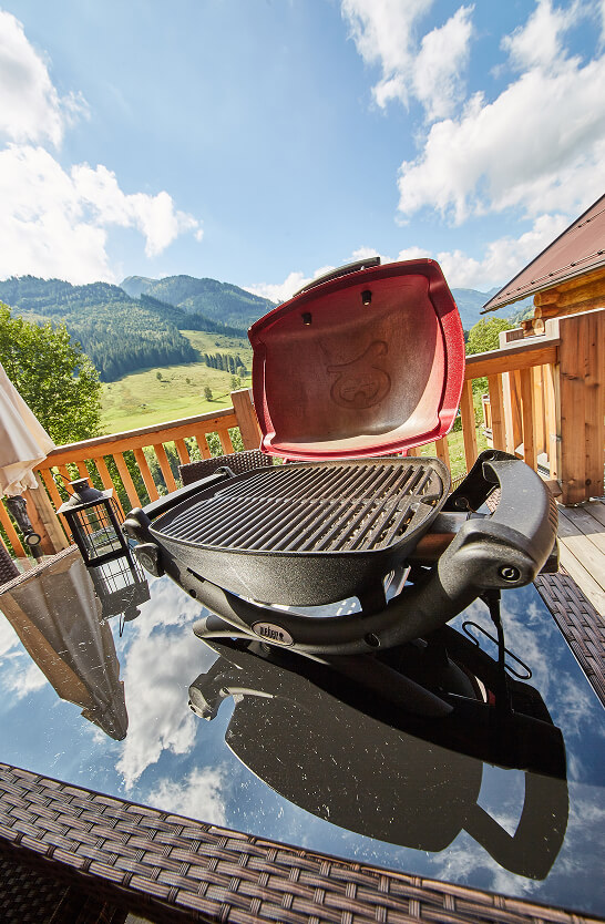 Offener Grill auf Balkon mit Bergblick und Himmel.