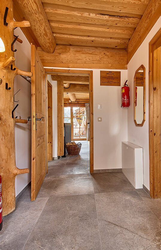 Flur mit Holzbalken, Fliesen, offener Tür, Feuerlöscher.