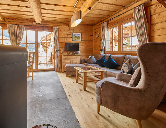 Blockhaus-Wohnzimmer mit Sofa, Sessel und Bergblick.