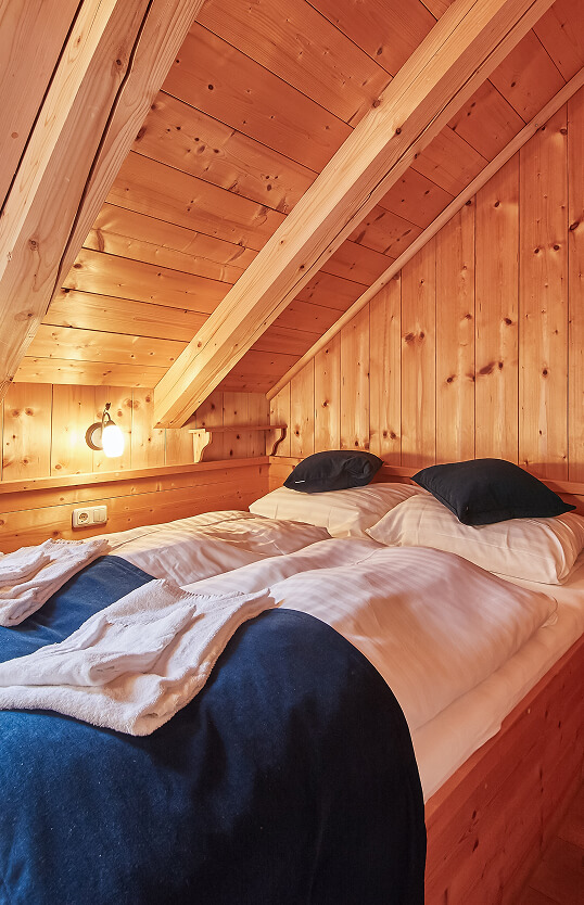 Zwei Betten in Holz-Dachzimmer mit Lampe.