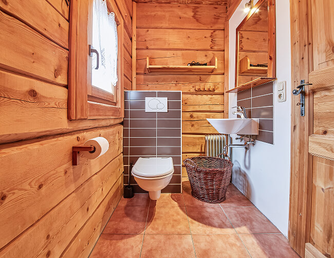 Toilette mit Holzwänden, Waschbecken, Spiegel, braunen Fliesen.