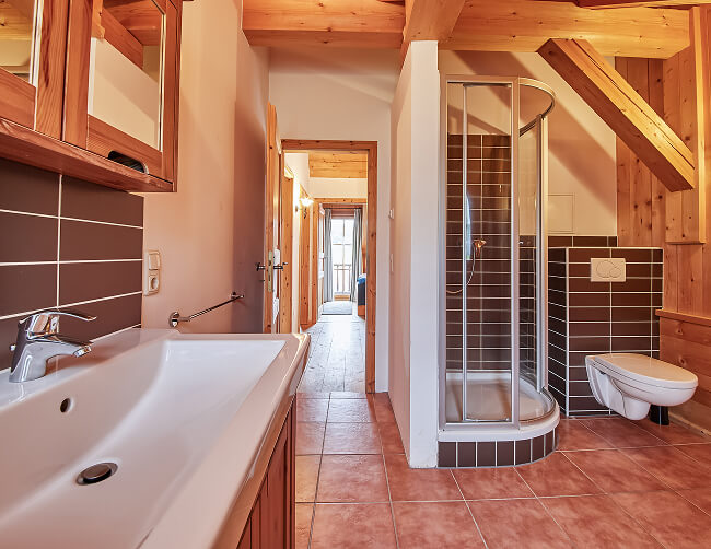 Bad mit Waschbecken, Dusche, WC. Braune Fliesen, Holz.