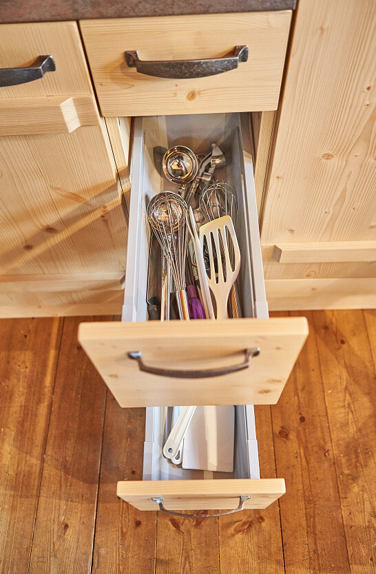 Zwei offene Holzschubladen, die obere voller Küchenutensilien.