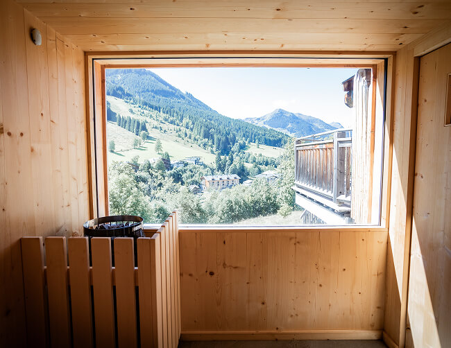 Blick aus Holzsauna auf grüne Berglandschaft.