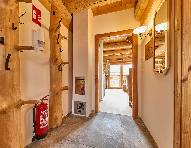 Flur mit Holzgarderobe, Feuerlöscher, Spiegel, offener Tür.
