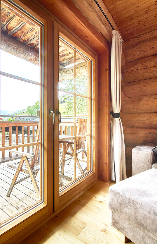 Blockhaus-Inneres mit Balkontür zu Stühlen und Bergblick.