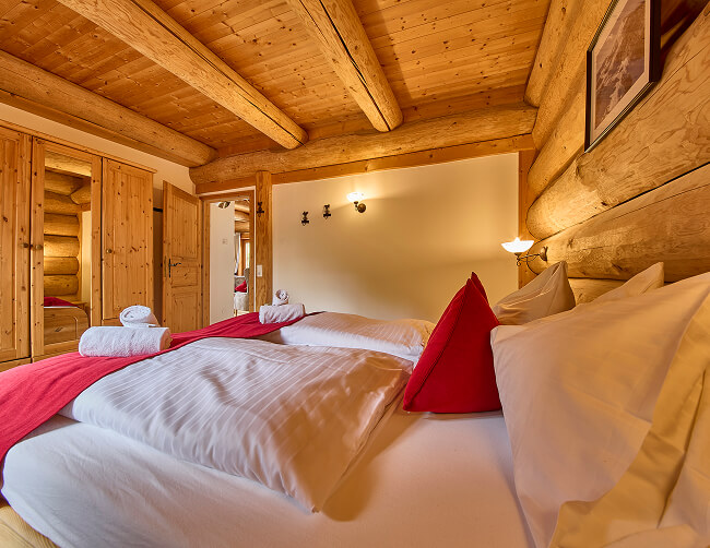 Schlafzimmer mit Holzwänden, weißem Bett, roter Decke.