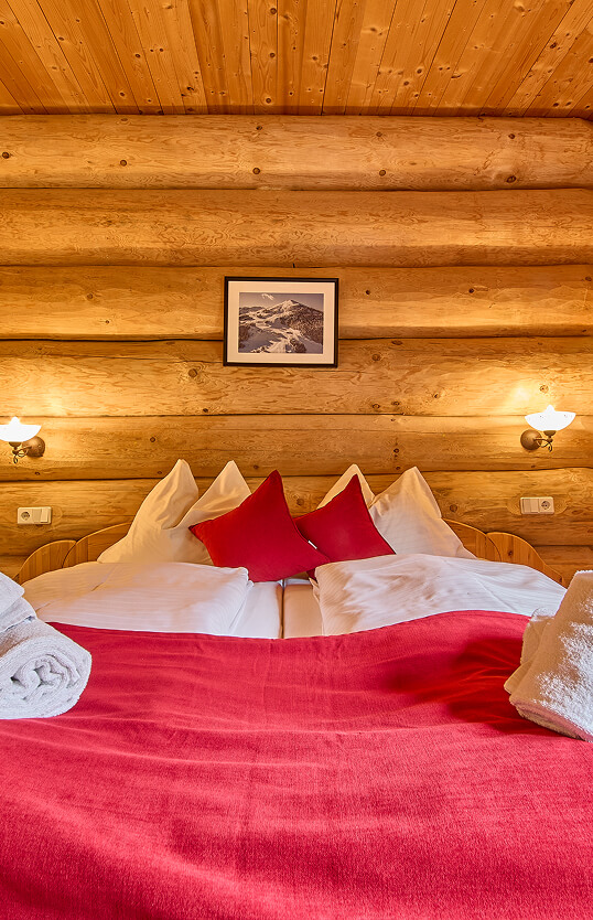 Doppelbett mit roter Decke in Blockhaus-Zimmer.
