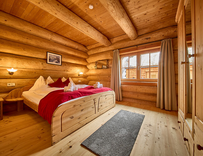 Schlafzimmer aus Blockholz mit Bett, Fenster, Schrank.