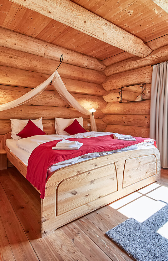 Schlafzimmer aus Holzstämmen mit Bett und rotem Bezug.