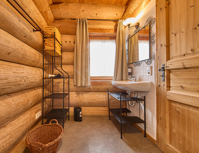 Blockhaus-Bad mit Waschbecken, Spiegel und Handtuchregal.