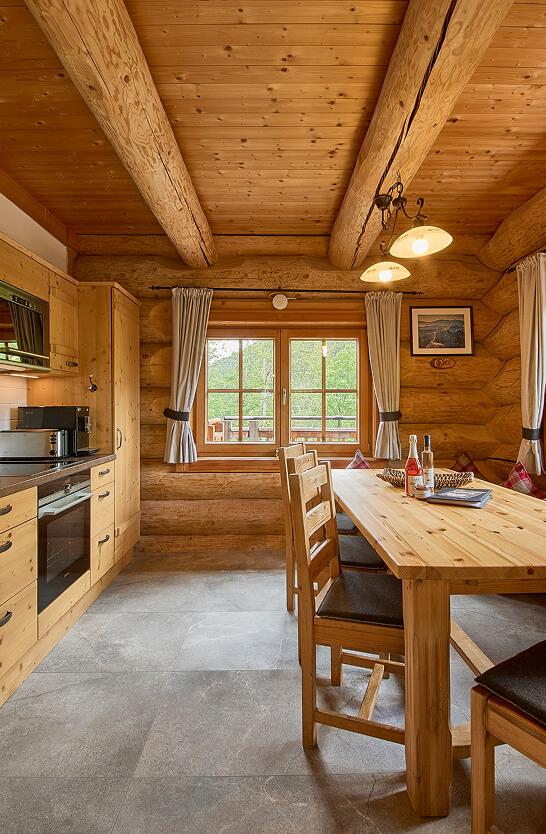 Holz-Wohnküche mit Esstisch und Blick ins Grüne.