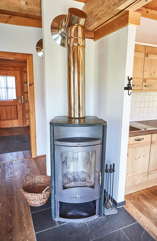 Grauer Holzofen mit Metallrohr, Korb, Holzboden und Küche.