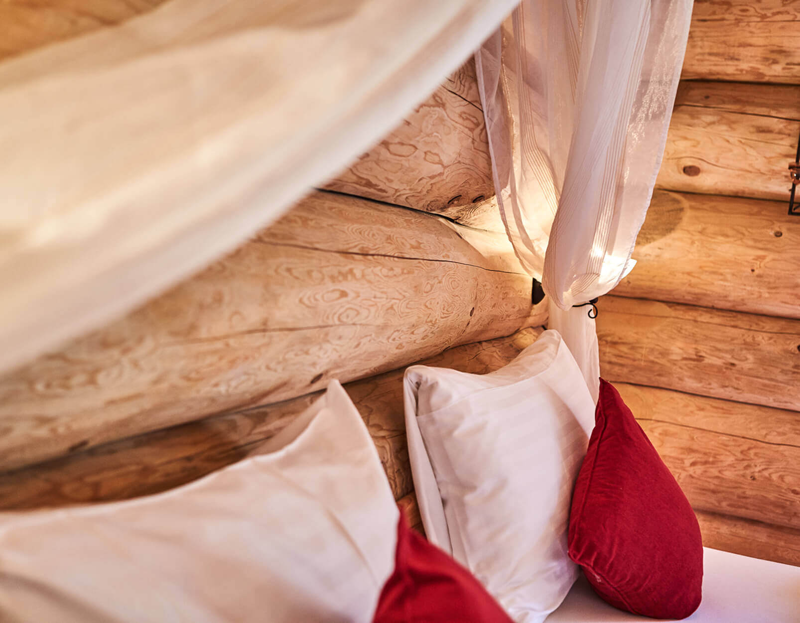 Nahaufnahme: Bett mit Kissen, Holzstammwand, transparentem Vorhang.