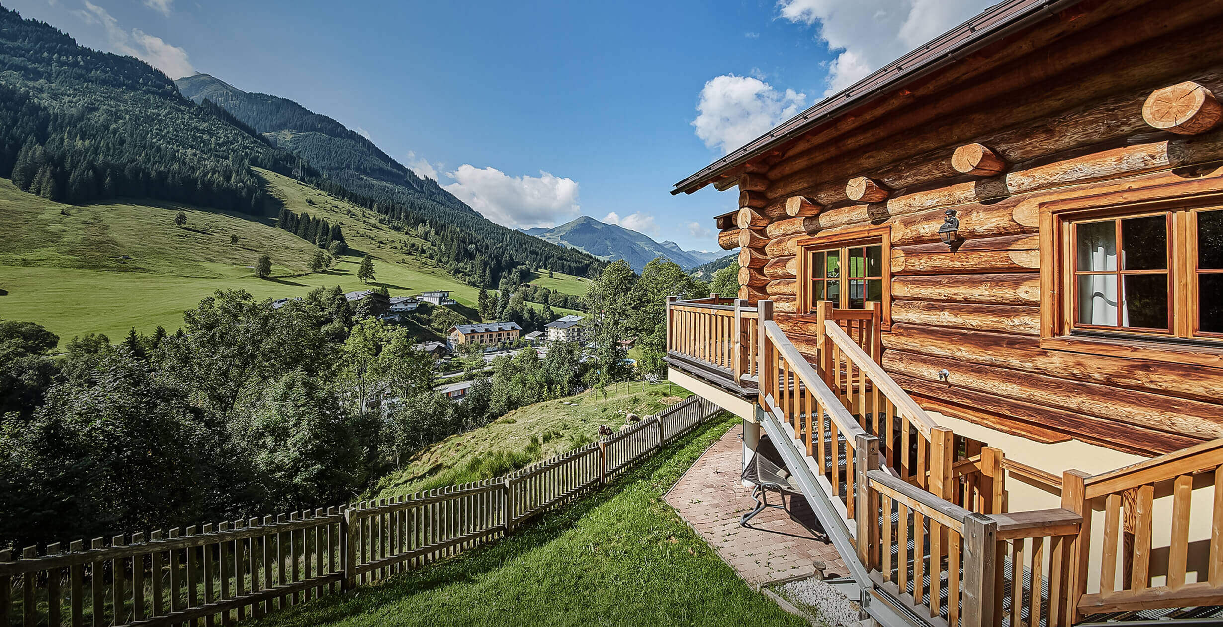 Blockhaus mit Holztreppe, Dorf im grünen Bergtal.