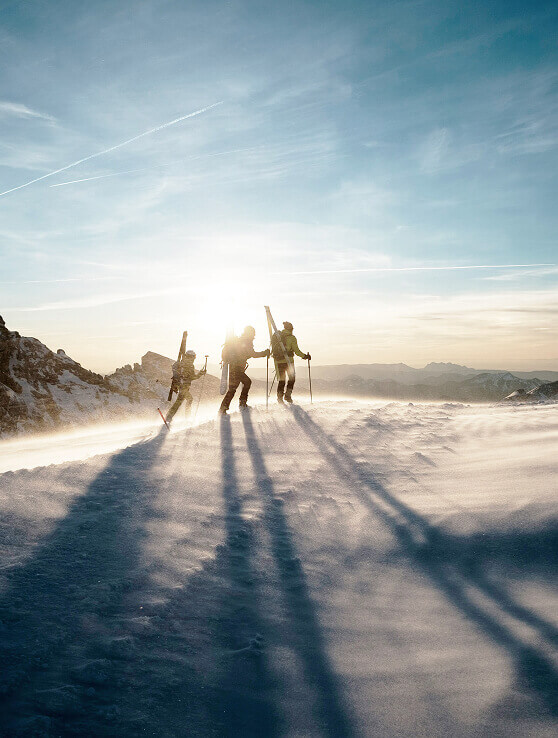 Drei Skitourengeher im Wind mit langen Schatten.