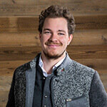 Lächelnder junger Mann vor Holzwand.