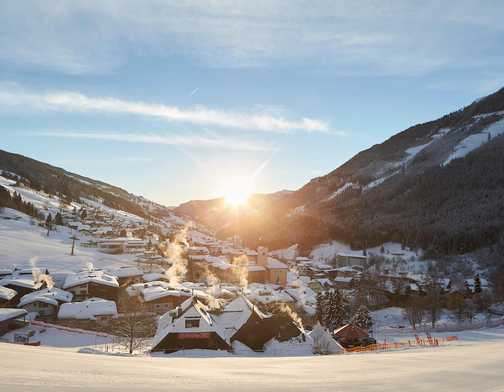 Sonnenuntergang über verschneitem Bergdorf, Kamine rauchen.