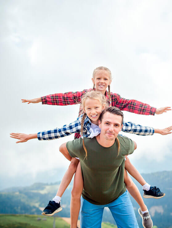 Mann mit zwei Mädchen übereinander, lächelnd, Arme seitlich.