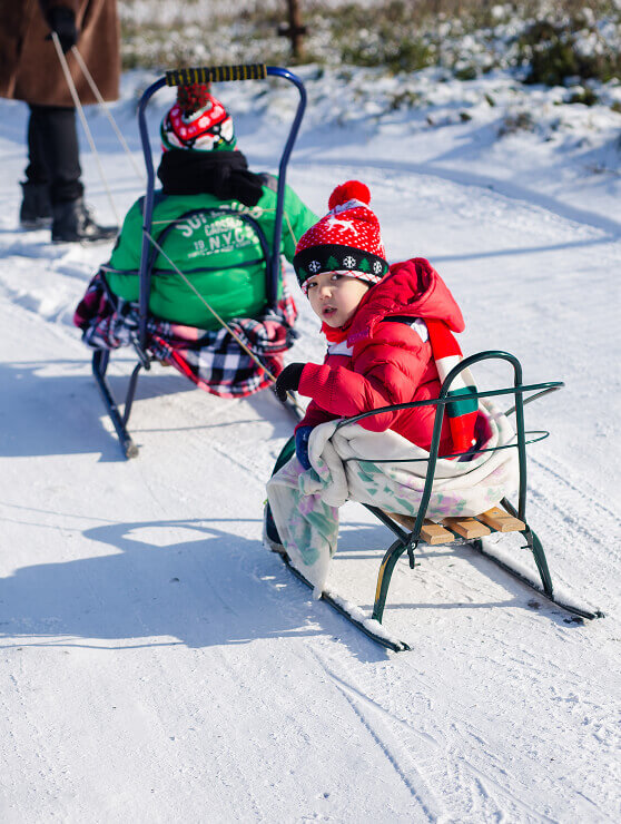 Zwei Kinder in Winterkleidung auf Schlitten im Schnee.