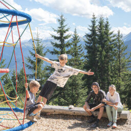 Zwei Jungen klettern, Erwachsene sitzen am Bergspielplatz.