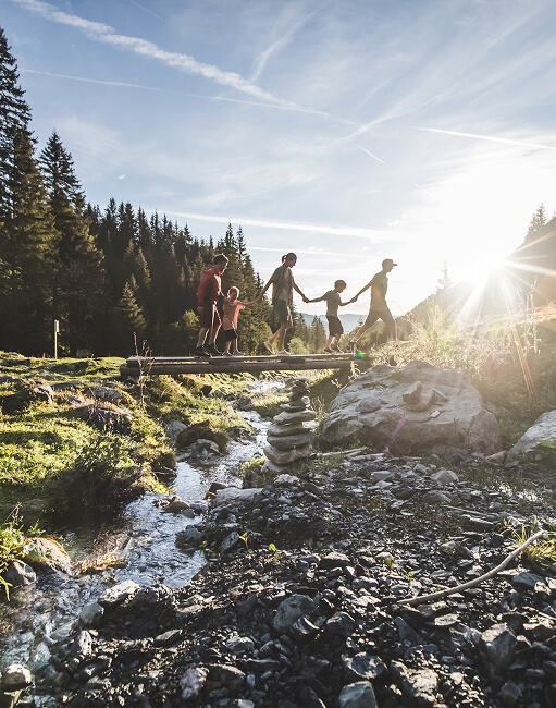 Familie überquert Brücke über Bach im Wald.