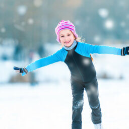 Lachendes Mädchen mit Mütze eislaufend auf dem Eis.