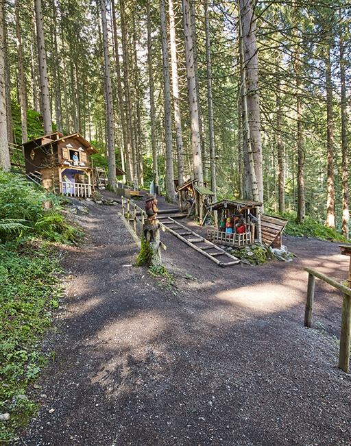 Waldpfad mit Holzhütten und Figuren.