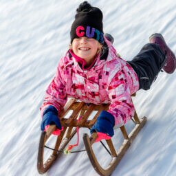 Lächelndes Kind rodelnd im Schnee.