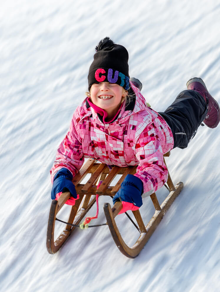 Lächelndes Kind rodelnd im Schnee.