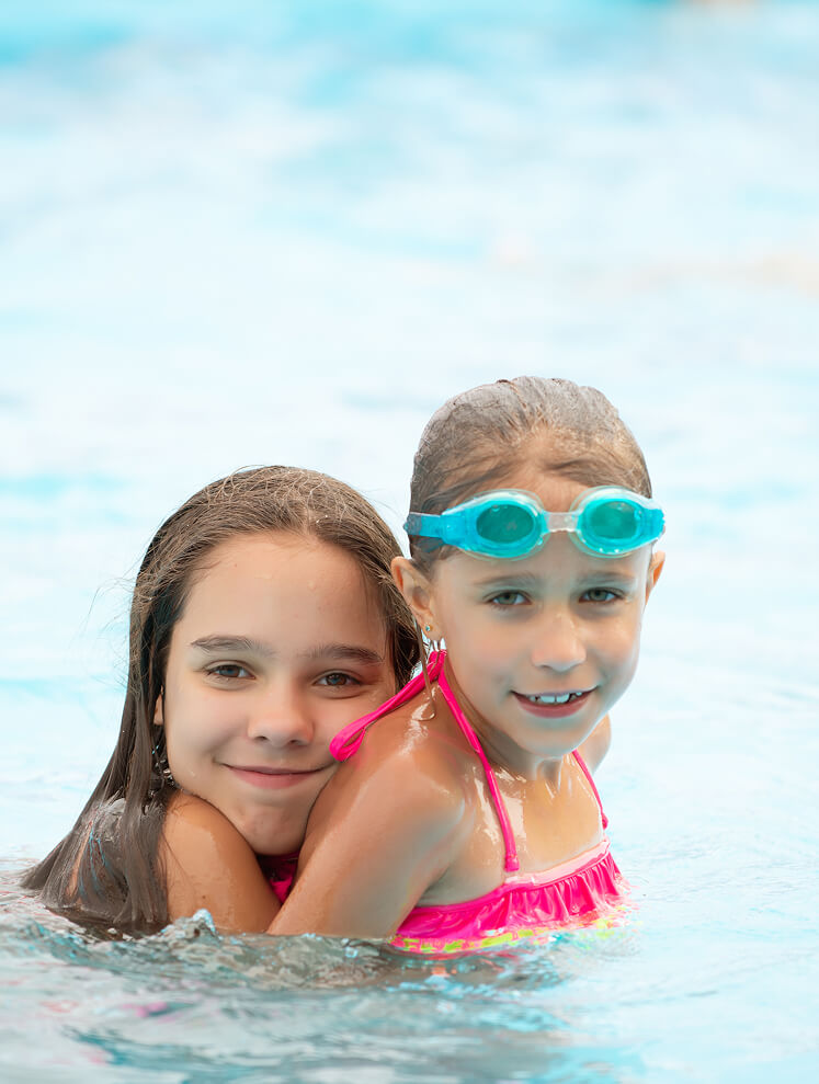 Zwei lächelnde Mädchen im Pool, eine mit Schwimmbrille.