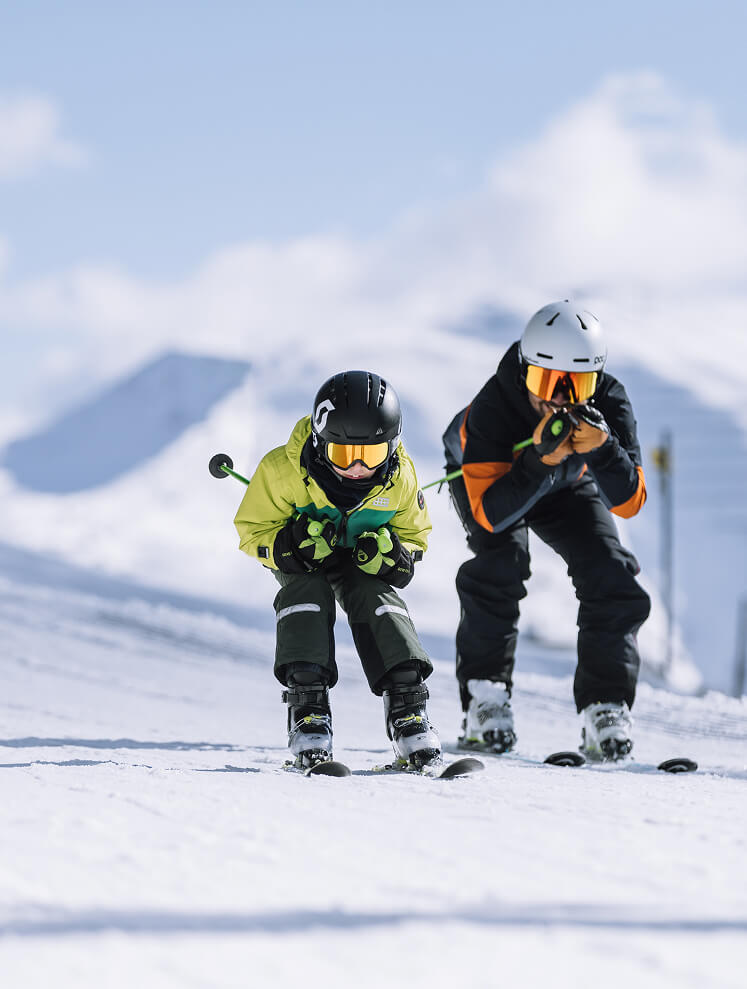 Zwei Skifahrer in Hocke auf verschneiter Piste.