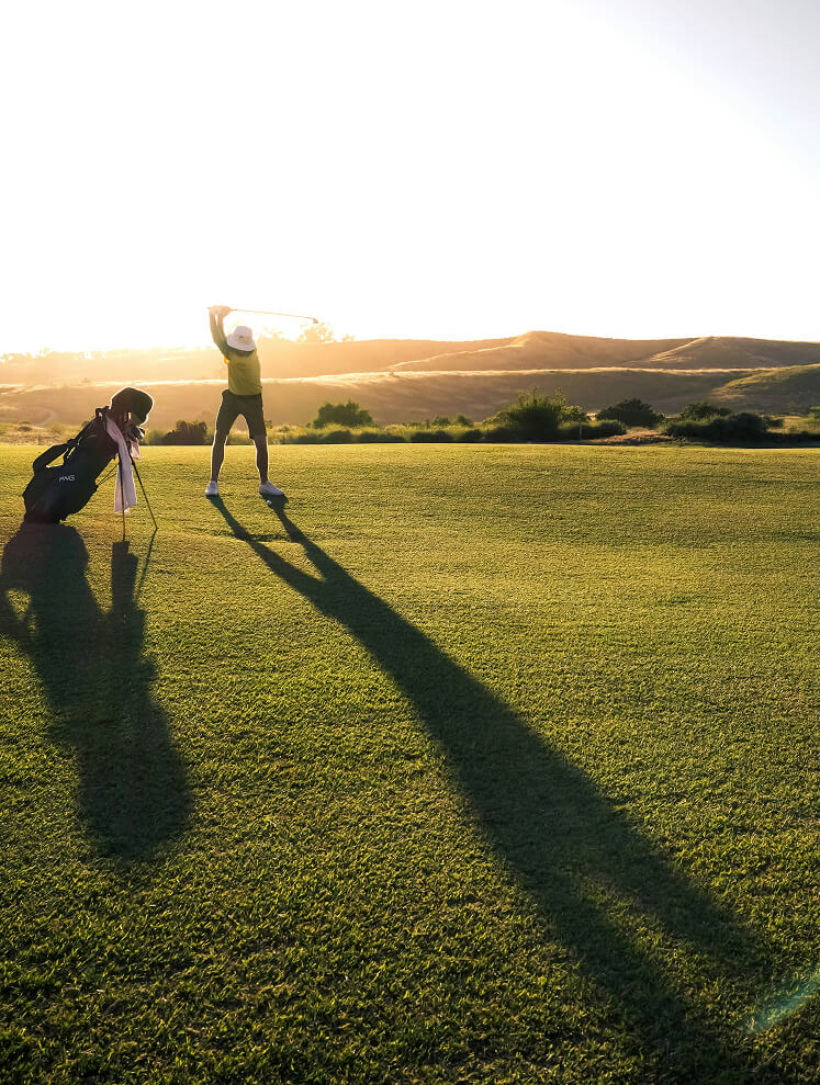 Golfer im Aufschwung, starkes Gegenlicht, lange Schatten.