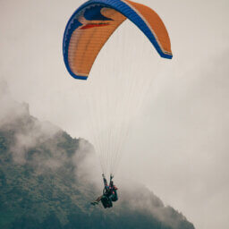 Zwei Menschen paragleiten vor nebeligen Bergen.