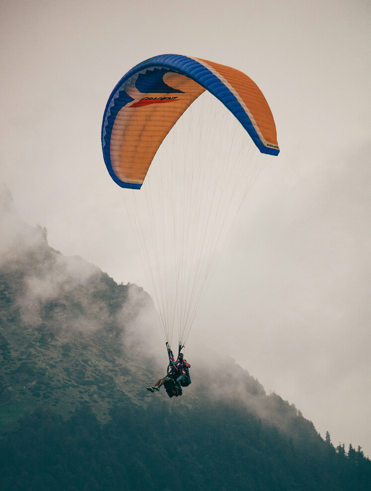 Zwei Menschen paragleiten vor nebeligen Bergen.