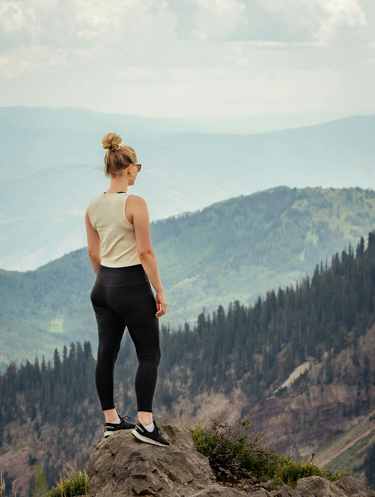 Frau blickt von Felsen auf Bergpanorama.