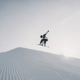 Snowboarder springt hoch über präparierte Piste.