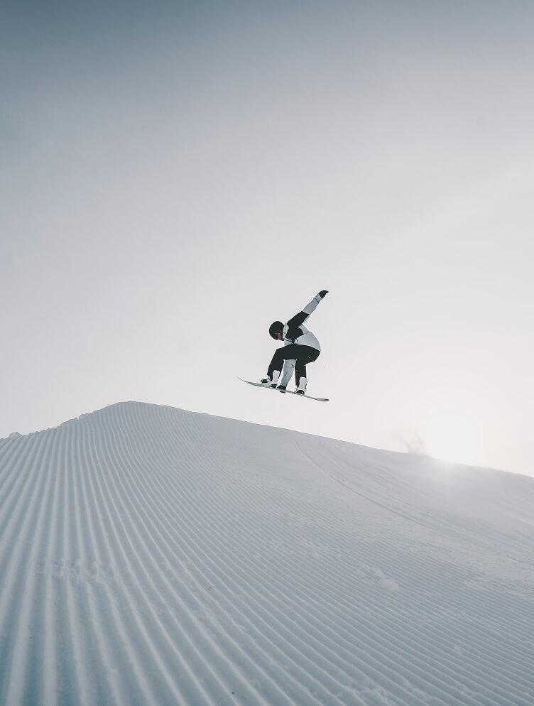 Snowboarder springt hoch über präparierte Piste.