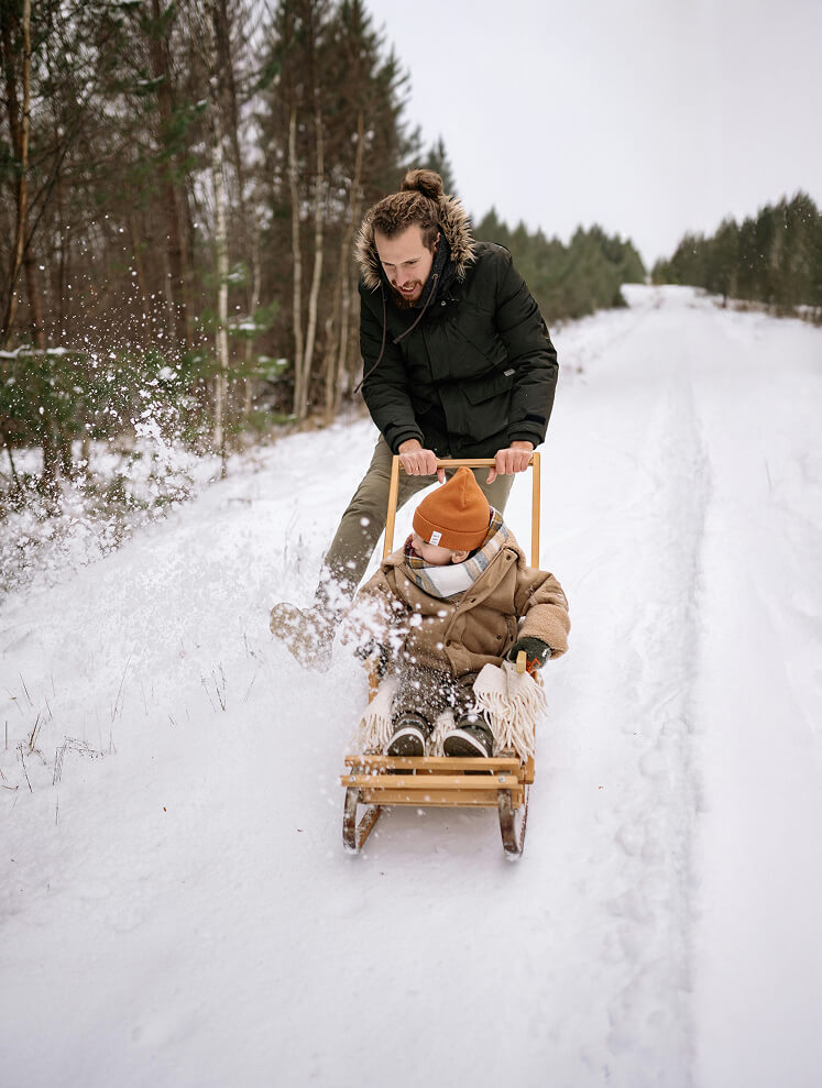 Mann schiebt Kleinkind auf Schlitten, Schnee spritzt.