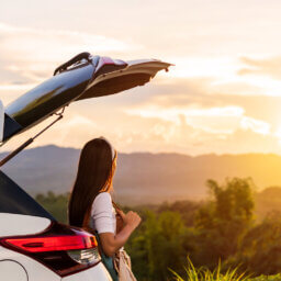 Person am offenen Kofferraum blickt in Sonnenuntergang.