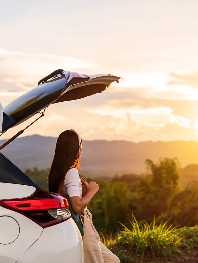 Person am offenen Kofferraum blickt in Sonnenuntergang.
