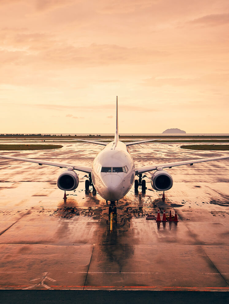 Weißes Passagierflugzeug auf nassem Rollfeld bei Dämmerung.