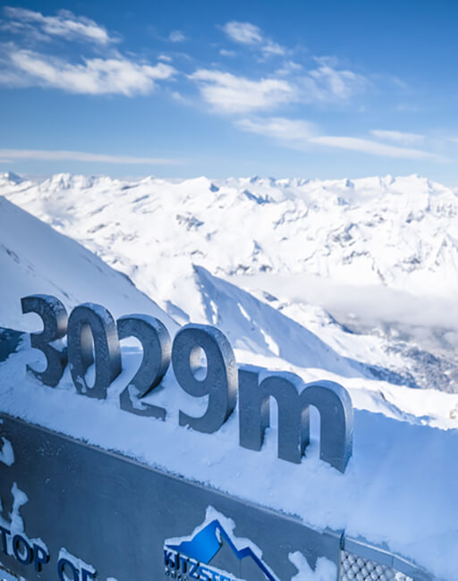 Schild mit '3029m' im Schnee vor verschneiter Berglandschaft.